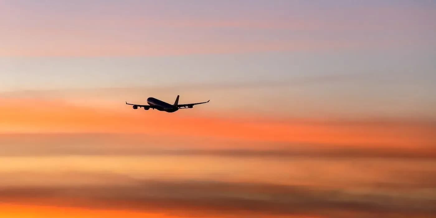 Commercial airplane silhouetted against vibrant orange and pink sunset sky