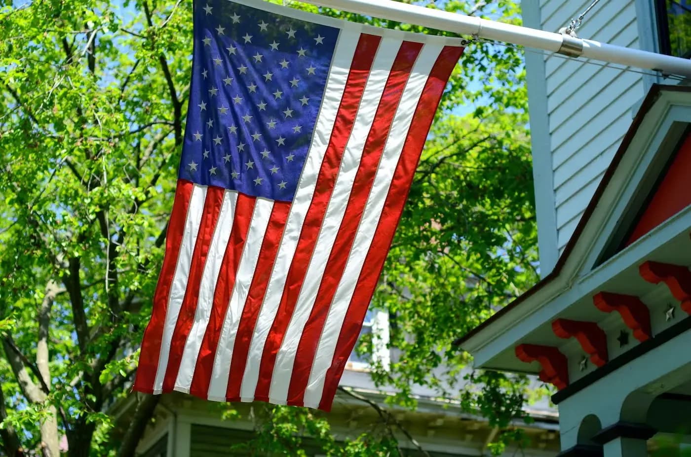 American flag hanging from residential home with green tree foliage in background