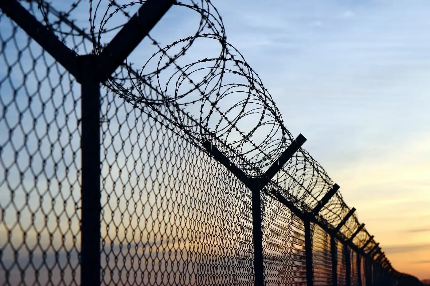 Silueta de una cerca de alambre de púas frente al cielo al atardecer, que simboliza la seguridad fronteriza y las barreras migratorias