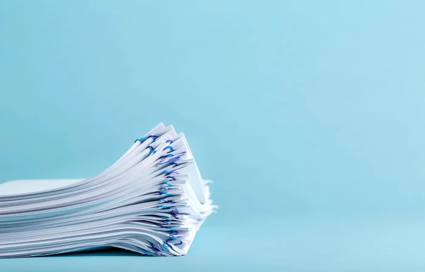 Pila de documentos oficiales con pinzas azules sobre un fondo azul claro