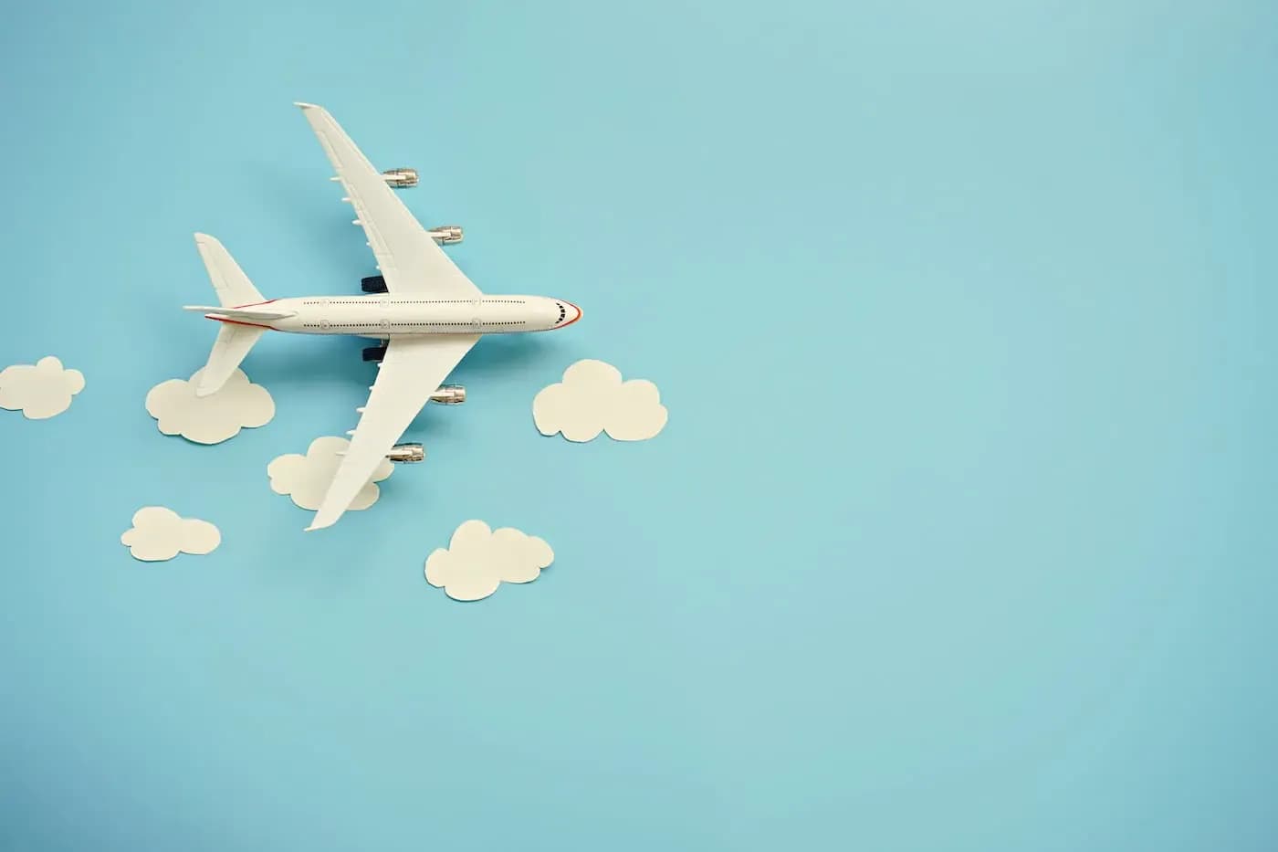 White airplane model flying among white clouds on light blue background