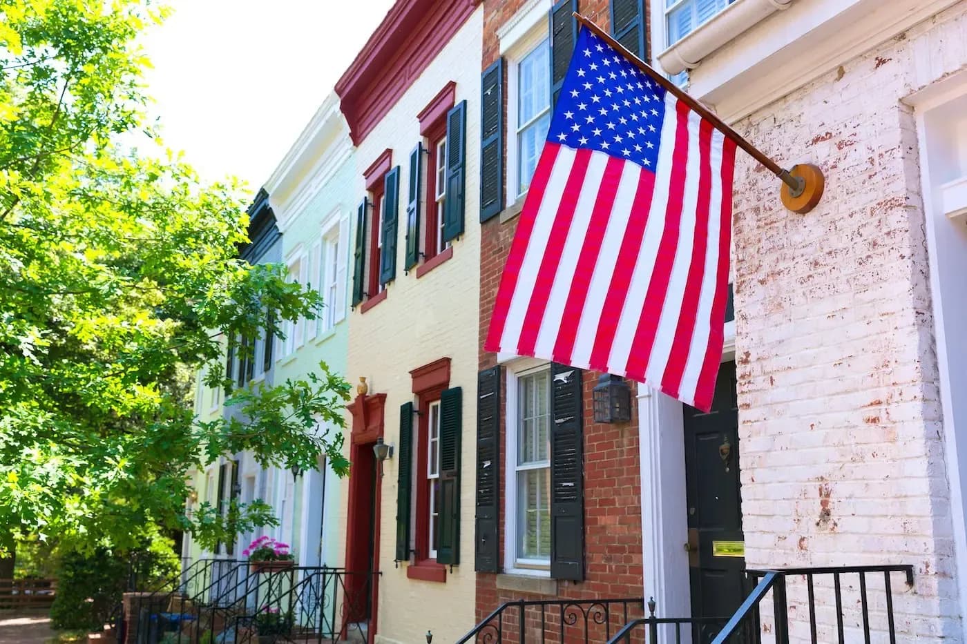 Large American flag hanging on historic brick building with colorful rowhouses on tree-lined street