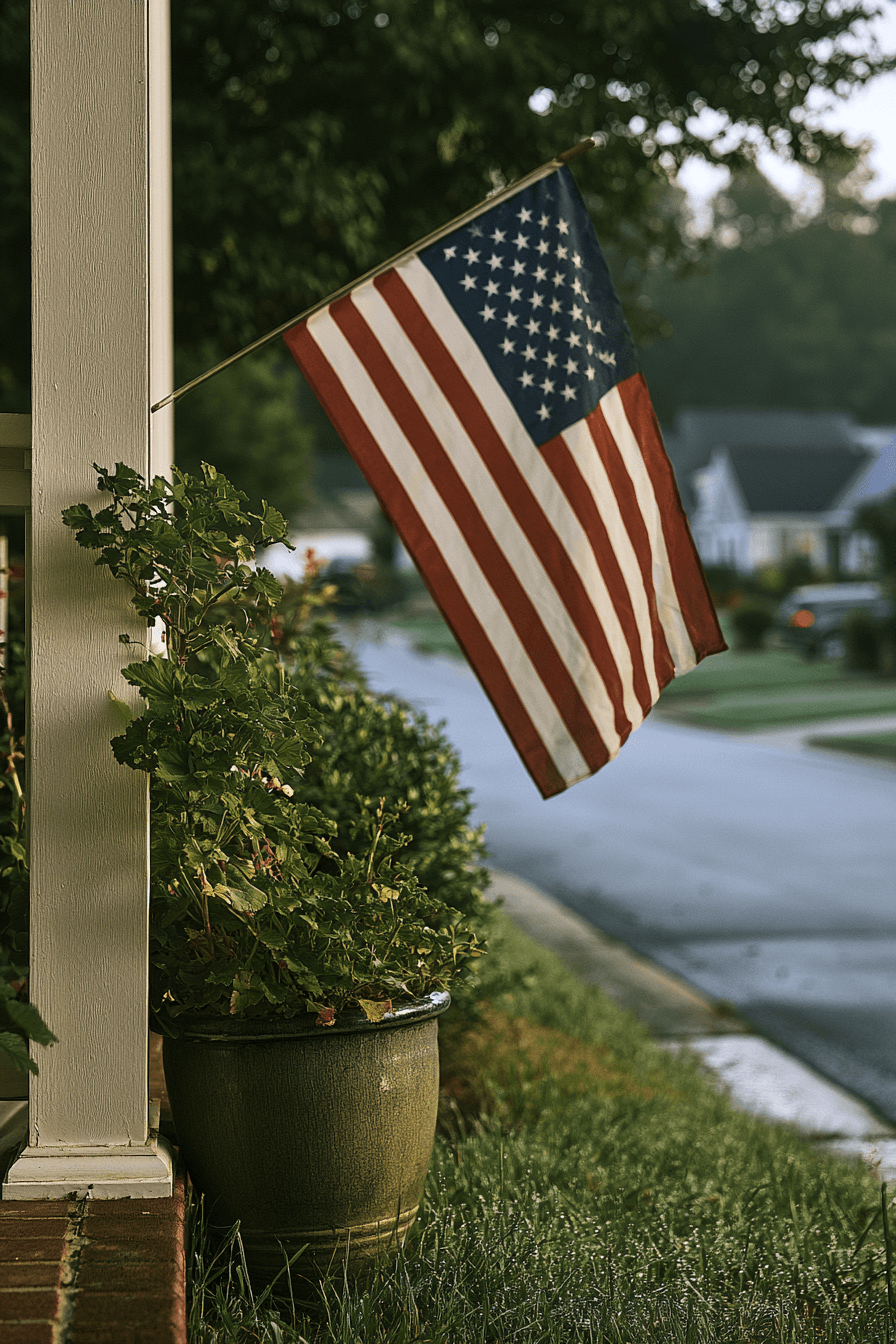 American flag hanging on a white column next to a potted plant outside a residential home