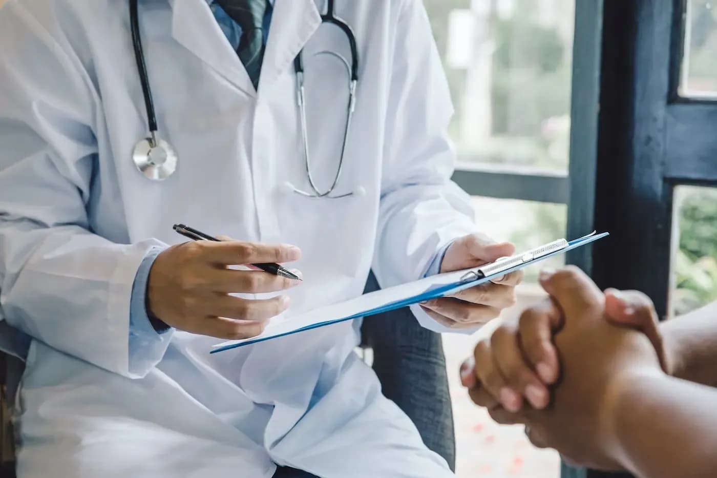 Profesional de la salud con bata blanca y estetoscopio revisando una carpeta junto a un paciente