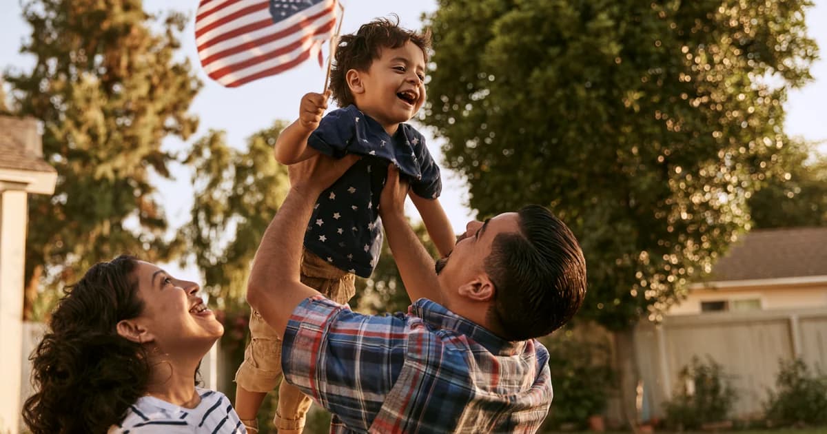Happy family of three holding an American flag outdoors in a residential neighborhood