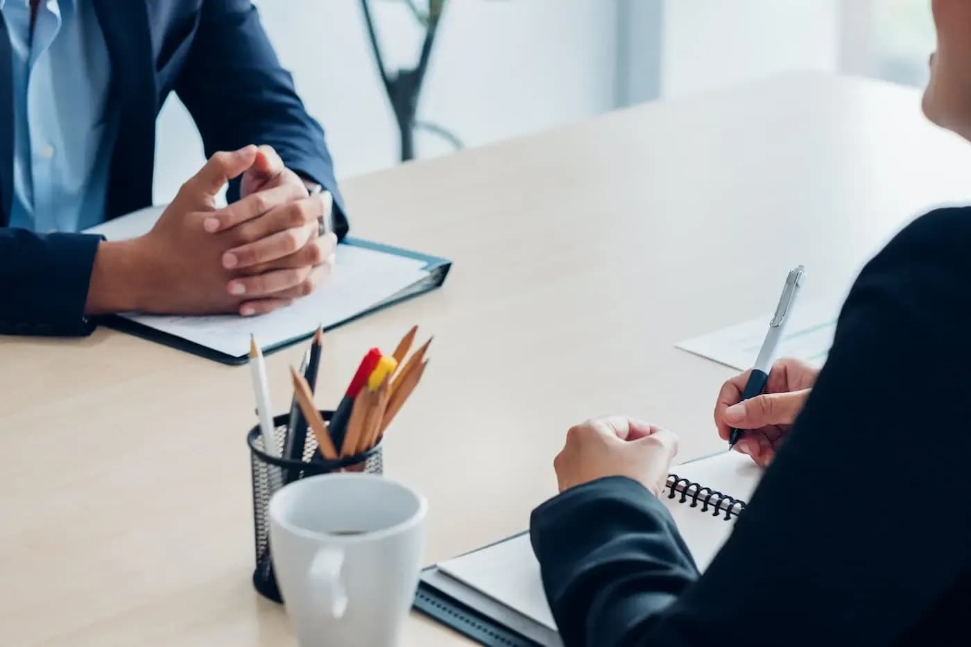 Two professionals in business attire engaged in a consultation at a desk with notebooks and writing materials