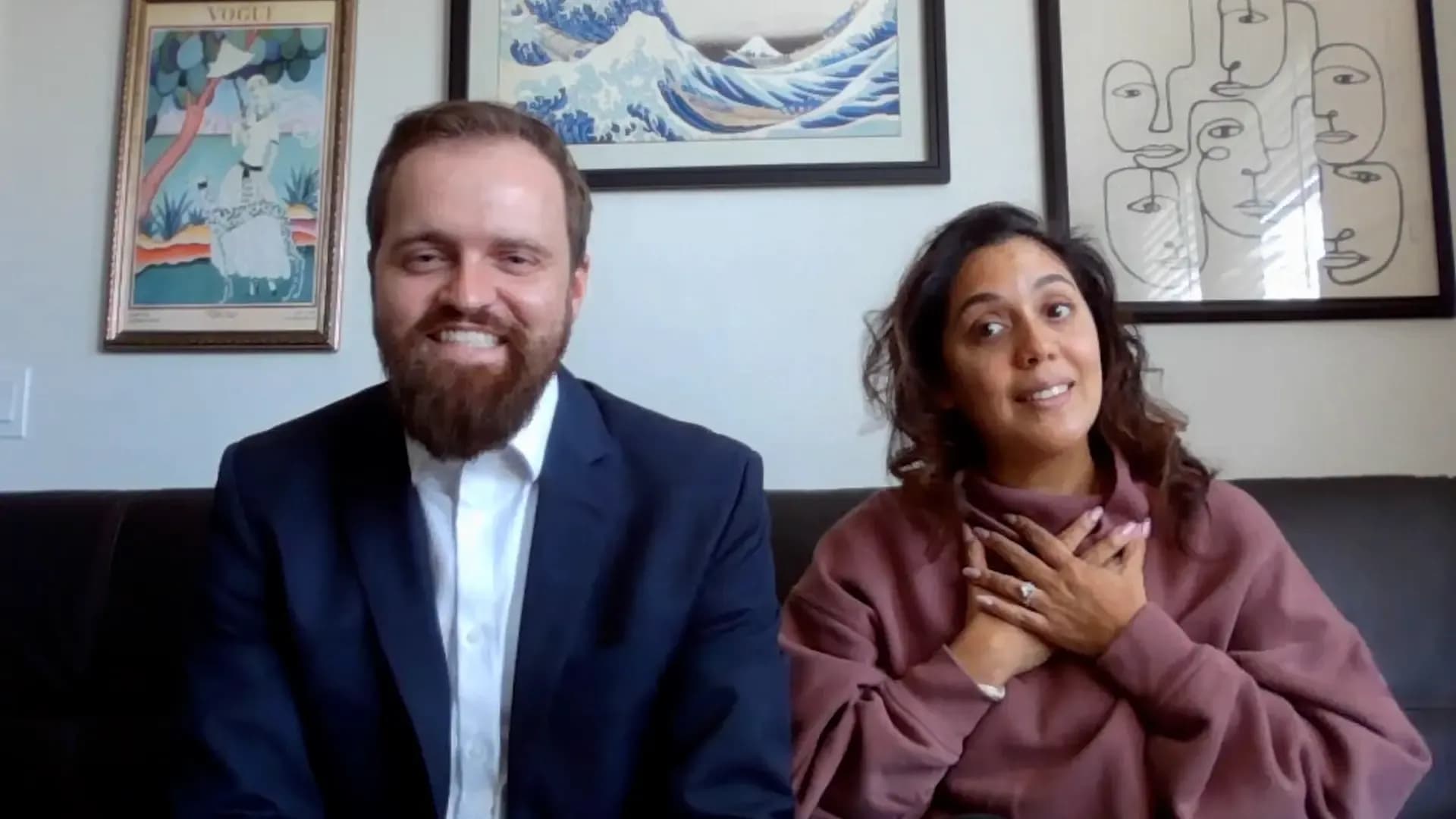 Two professionals sitting together in an office with framed artwork on the wall behind them