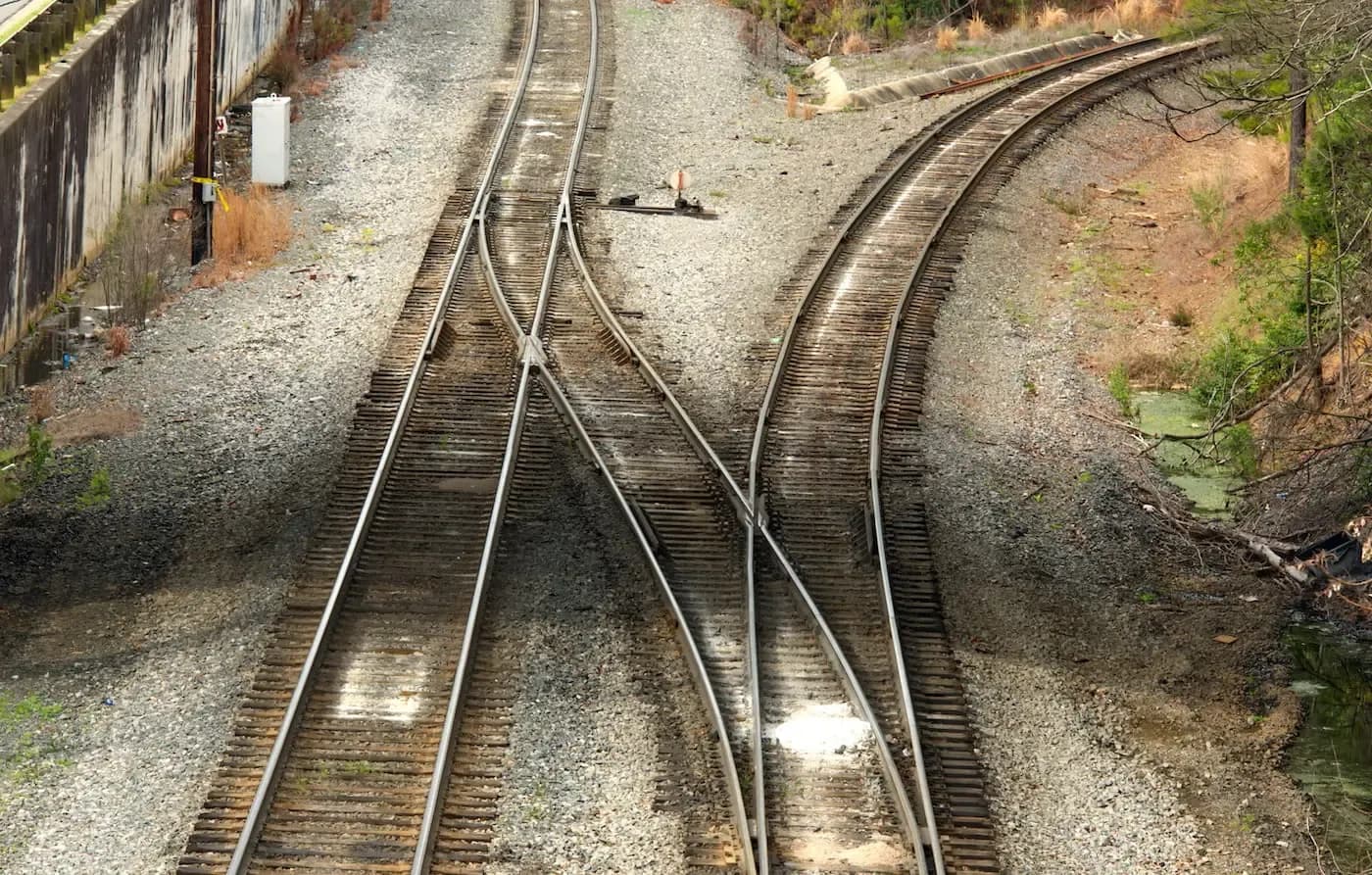 Multiple railroad tracks converging at a railway junction with gravel and vegetation