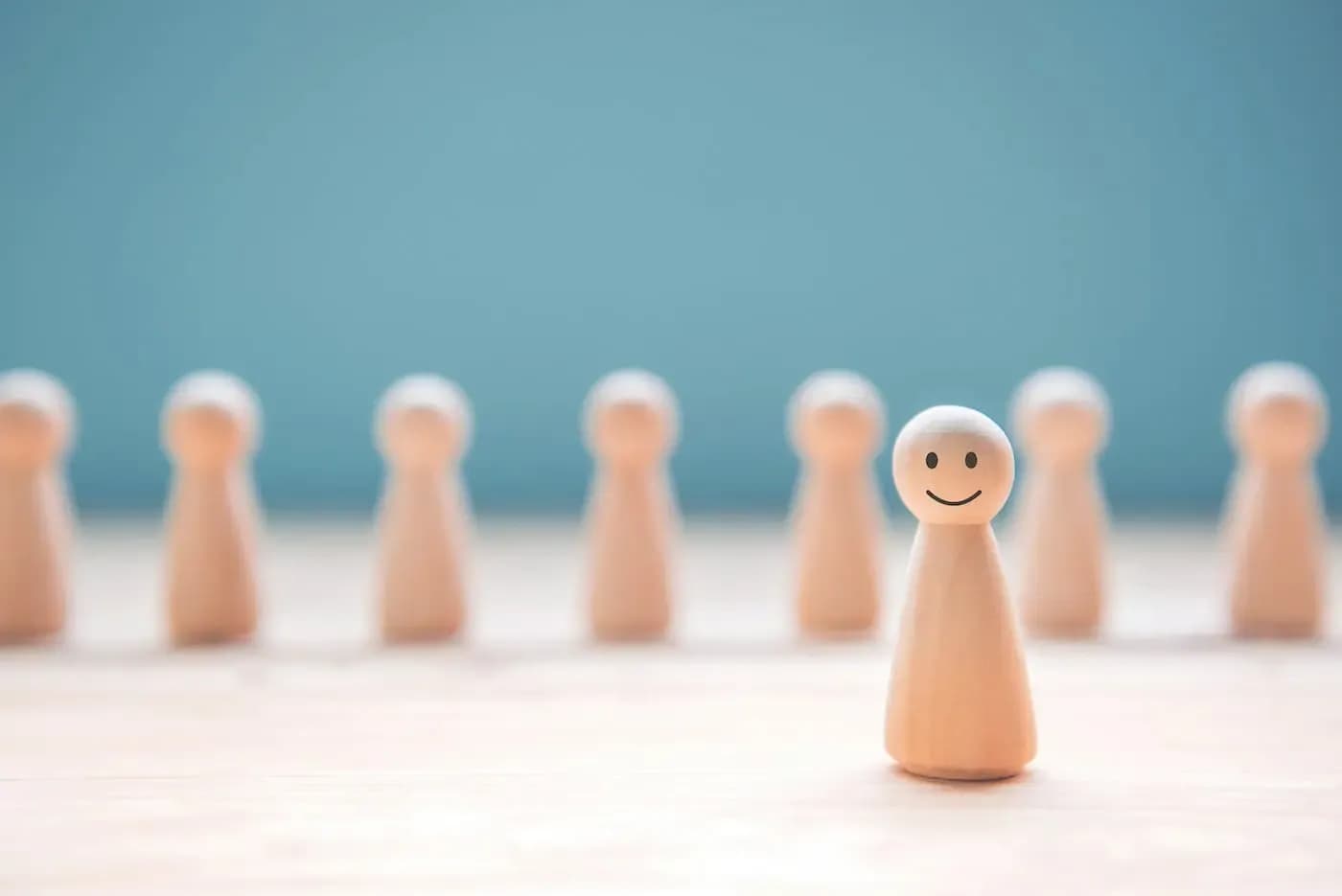 Wooden peg figure with smiling face stands out among blurred plain figures against blue background