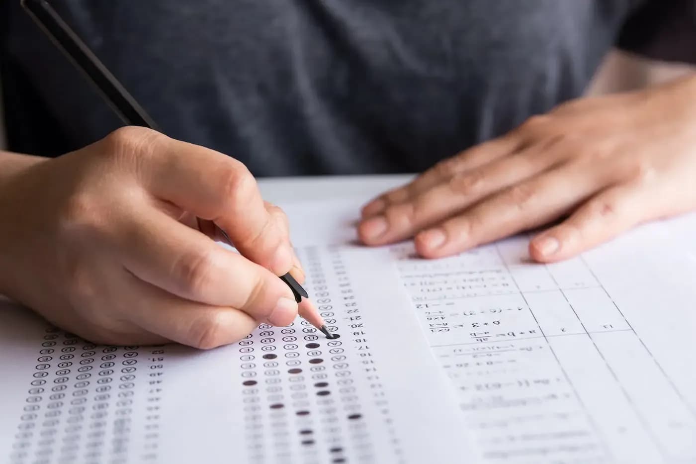 Close-up of a student's hands filling out a multiple choice test form with a pencil