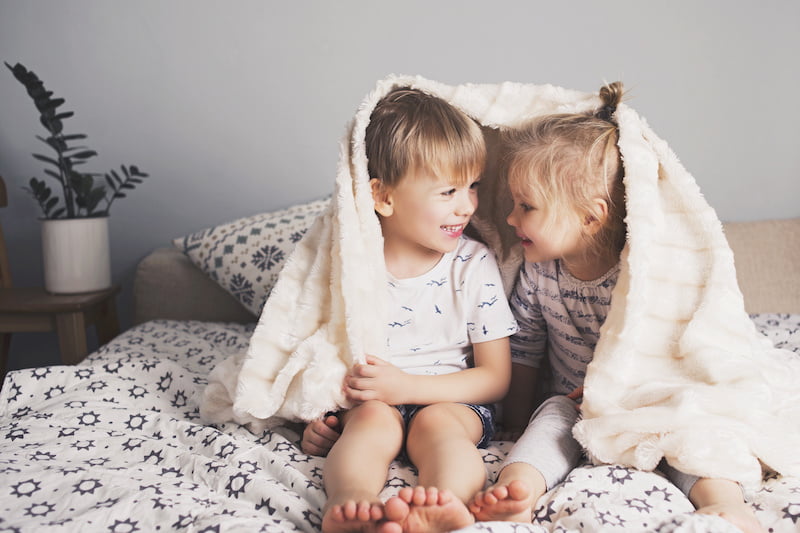 Two pretty smiling kids embrace under blanket