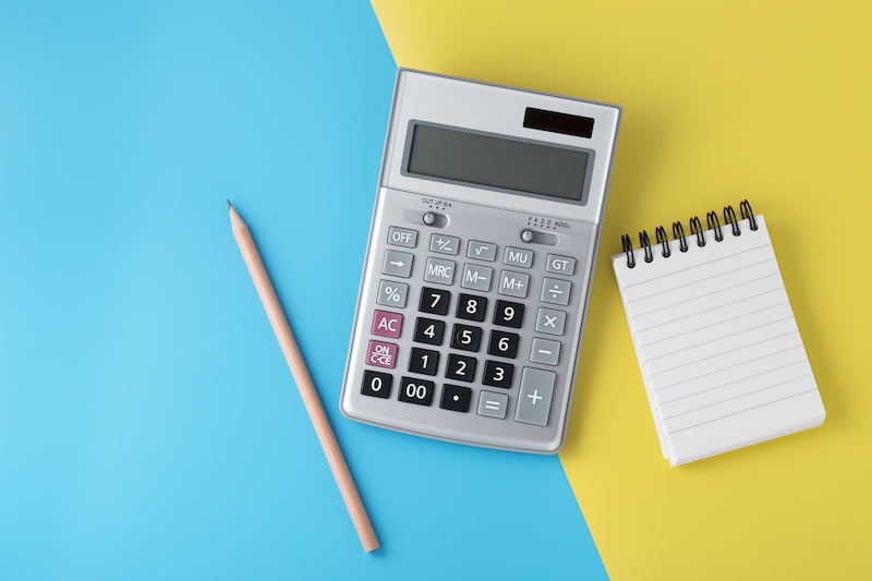 Calculator on light blue and yellow background with notepad and pencil, flat lay with space