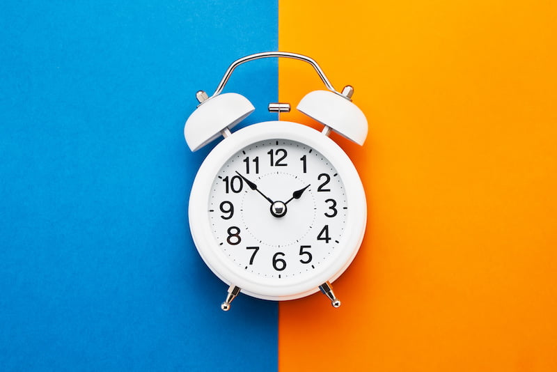 White vintage alarm clock on blue-orange background.