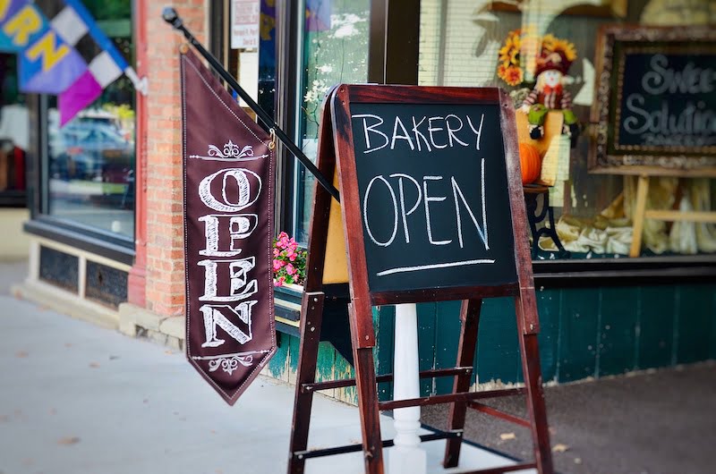 A wooden sign outside a bakery with "Bakery Open" written on it.